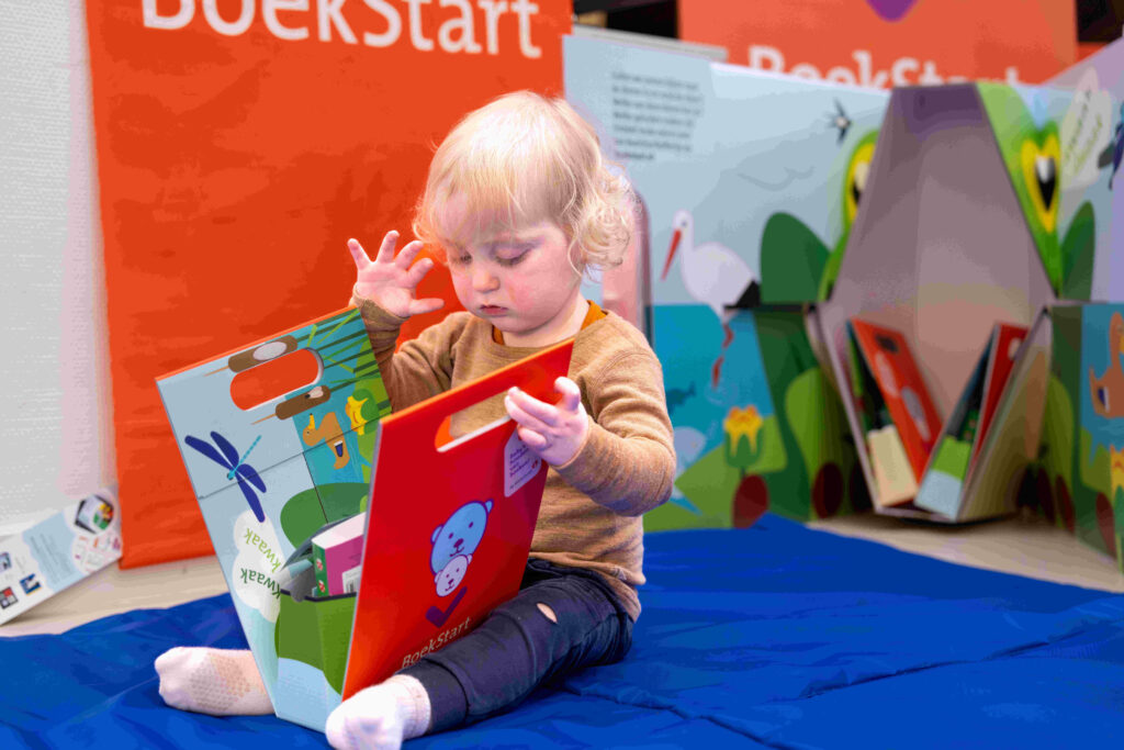 Kind open nieuwe BoekStarrkoffertje op de grond, in de achtergrond: een grote versie van de koffer.